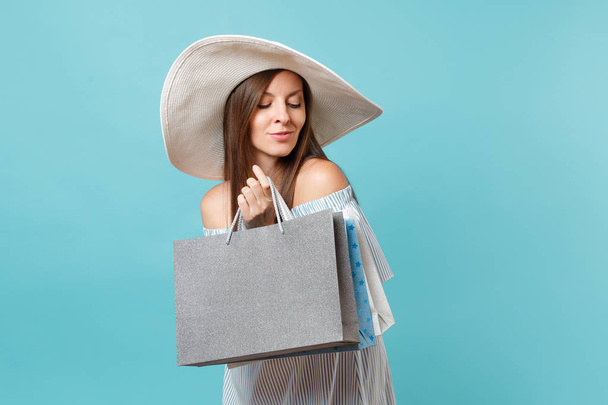 Portrait fashionable elegant fashion beautiful caucasian woman in summer dress, white large wide brim sun hat holding packages bags with purchases after shopping isolated on blue pastel background - Foto, Imagen