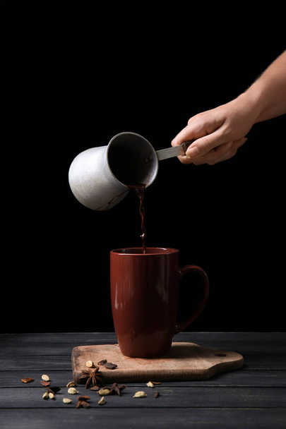 Frau gießt heiße Schokolade aus Cezve in Tasse auf Holztisch - Foto, Bild