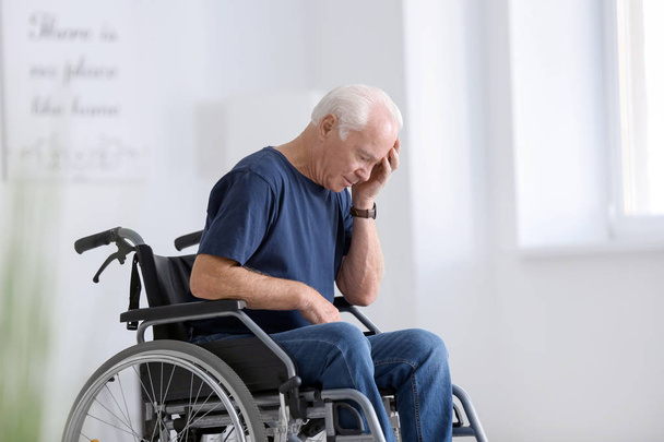 Hombre mayor discapacitado en silla de ruedas con dolor de cabeza en casa
 - Foto, imagen