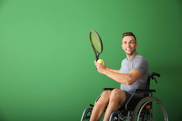 Спортивний молодий чоловік з тенісною ракеткою і м'ячем сидить у інвалідному візку на кольоровому фоні
 - Фото, зображення