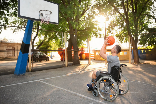 Νεαρός άνδρας σε αναπηρικό καροτσάκι να παίζει μπάσκετ σε εξωτερικούς χώρους - Φωτογραφία, εικόνα
