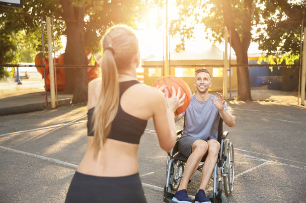 Young man in wheelchair and sporty woman training with ball outdoors - Photo, Image