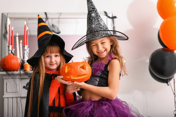 Милые маленькие девочки в костюмах на Хэллоуин и с Джеком-фонариком дома
 - Фото, изображение