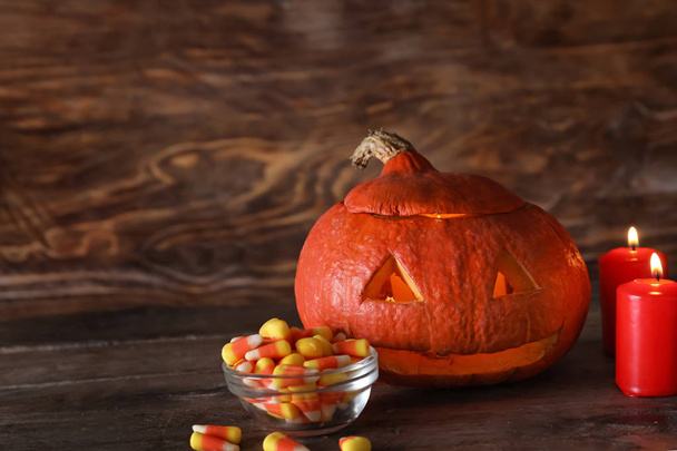 Zucca di Halloween con caramelle e candele accese su sfondo di legno
 - Foto, immagini