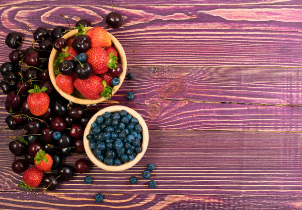 Čerstvé červené třešně, borůvky a jahody na staré dřevěné pozadí s copy prostor pro design fotomontáž nebo makety. Rustikální dřevěný stůl stůl struktura s sladké bobule zblízka a pohled shora - Fotografie, Obrázek