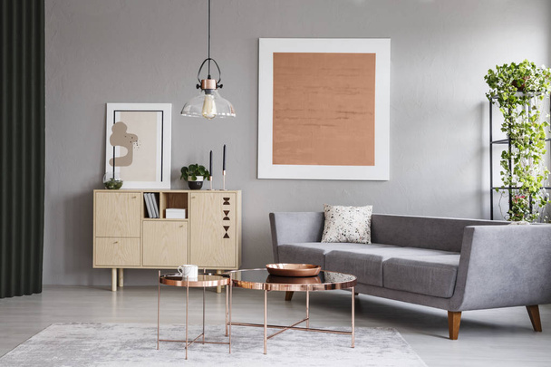 moderne Couch und Kupfertische in einem grauen Wohnzimmer-Interieur mit einem Gemälde. echtes Foto - Foto, Bild