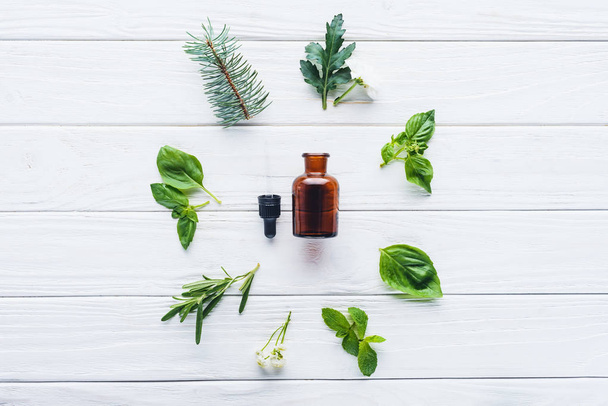 вид сверху на бутылку натурального растительного эфирного масла, капельницу и зеленые растения на белом деревянном столе
 - Фото, изображение