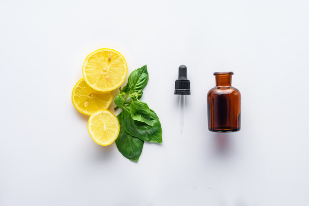 vista superior de la botella de aceite esencial de hierbas naturales, gotero, trozos de limón y hojas verdes aisladas en blanco
 - Foto, Imagen