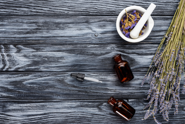 верхний вид бутылок натуральных травяных эфирных масел, капельницы и сушеных цветов на деревянный стол
 - Фото, изображение