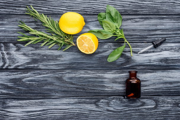 elevated view of bottle of natural herbal essential oil, dropper and lemons on wooden table - Photo, Image