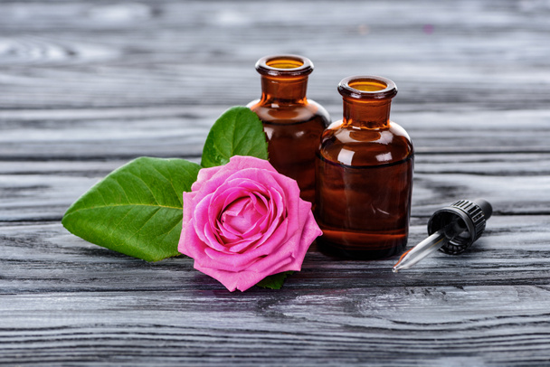 μπουκάλια φυσικά φυτικά αιθέρια έλαια, σιφώνιο και ροζ τριαντάφυλλο σε ξύλινη επιφάνεια - Φωτογραφία, εικόνα