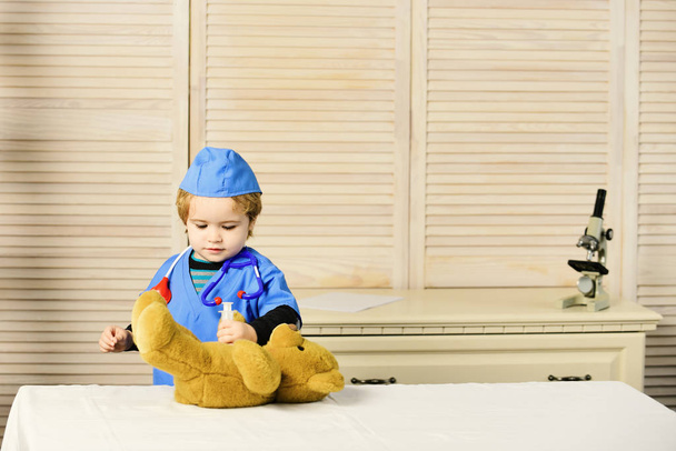 Kid in doctor coat makes injection to teddy bear. - Foto, Imagen