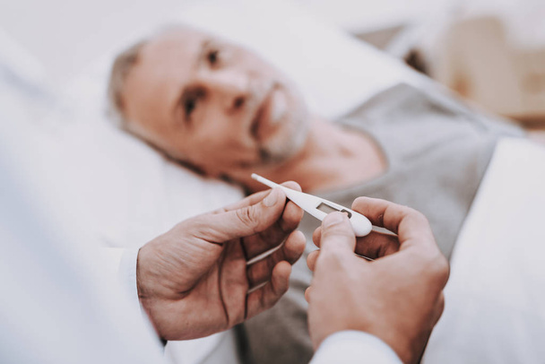 Thermometer and Patient. Old man Lies in Hospital. Nurse and Doctor Help Patient. White Room and Patient. Therapy for Patient in a Clinic. Care Doctor and Nurse. Rehabilitation and Therapy for Patient - Foto, imagen