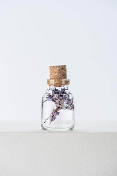 白い表面に紫の花を持つ天然ハーブのエッセンシャル オイルのボトル - 写真・画像