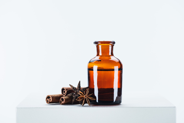 bottle of natural herbal essential oil and carnation with cinnamon sticks on white cube - Photo, Image