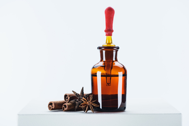 botella de aceite esencial de hierbas naturales, gotero y clavel con palos de canela en cubo blanco
 - Foto, Imagen