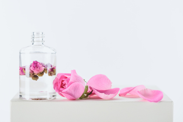 bottle of aromatic essential oil with pink roses on white surface - Photo, Image