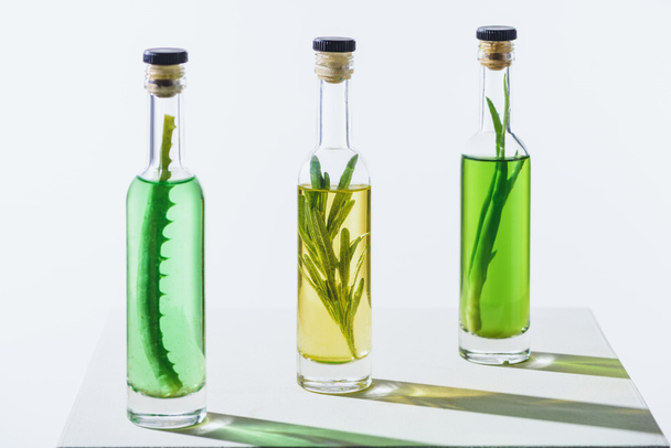 μπουκάλια βασικά έλαια πράσινο και κίτρινο με φυτά σε λευκή επιφάνεια - Φωτογραφία, εικόνα