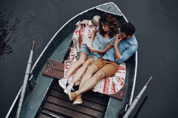 beautiful young woman reading book while lying in boat with boyfriend - Photo, image