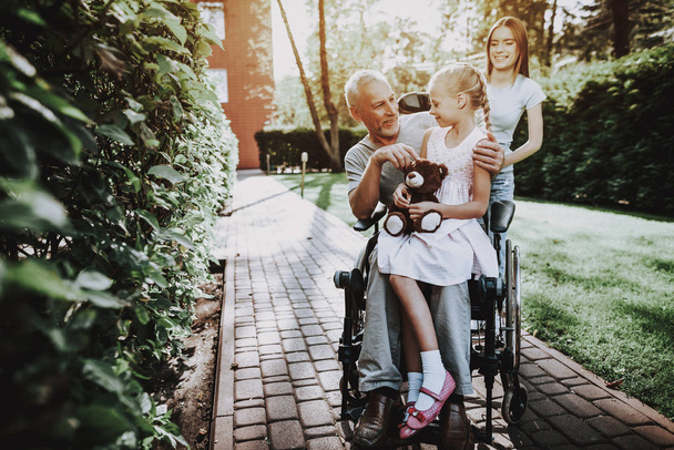 Aged Man with Girl. Girl with Bear on Stroller. Businessman in Stroller with Happy Child. Smile all Family. Rehabilitation With Wheelchair. Caregiver with Old Man and Child. Together Happy Family. - Fotografie, Obrázek