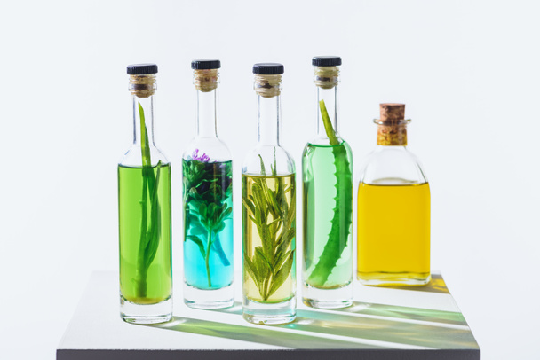 bottles of aromatic essential green and yellow oils with herbs on white cube - Fotó, kép