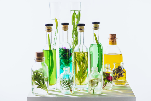different glass bottles of natural herbal essential colored oils on white cube - Fotografie, Obrázek