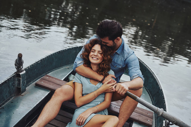 happy couple embracing and smiling while enjoying romantic date on lake in boat - Foto, Bild