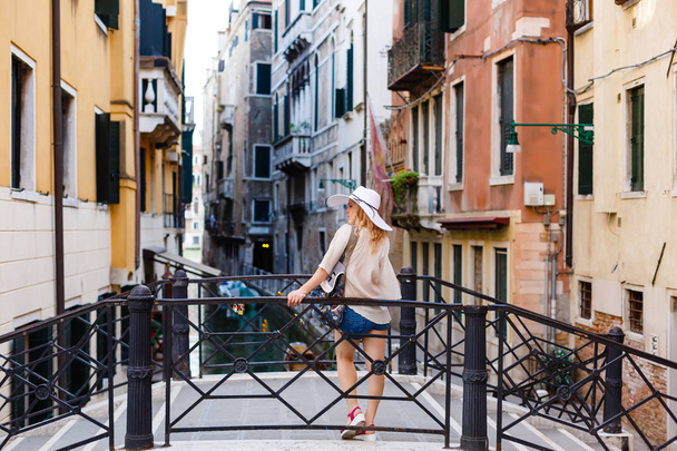 Woman tourist travel in Italy. Young girl with a white hat in venice on an old street. Girl traveling to Venice. - 写真・画像