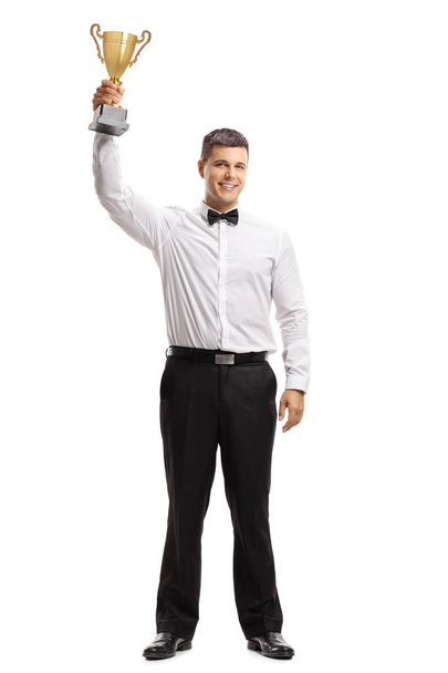 Full length portrait of a young man in a tux holding a golden trophy isolated on white background - Fotó, kép