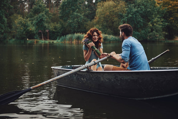 beautiful young woman holding bouquet of flowers while enjoying romantic date on lake in boat with boyfriend - Fotó, kép