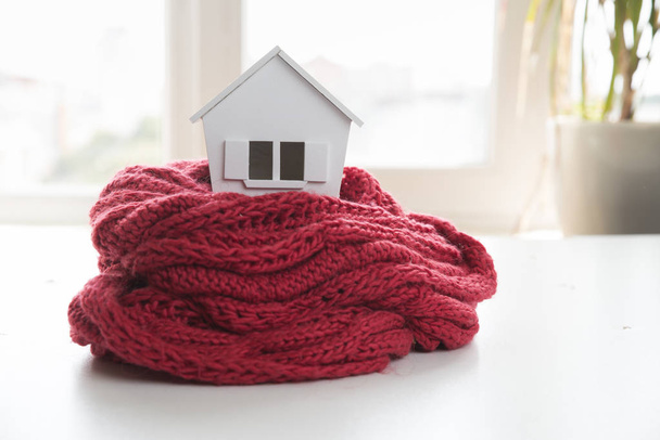 huis in de winter - verwarming systeemconcept en koude besneeuwde weer met model van een huis, het dragen van een gebreide cap - Foto, afbeelding