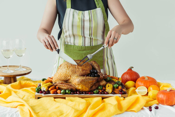 vista parcial de la mujer en delantal corte pavo asado para la cena de Acción de Gracias vacaciones sobre fondo gris
 - Foto, Imagen