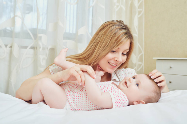 Una madre feliz con un bebé juega en una cama
.  - Foto, imagen
