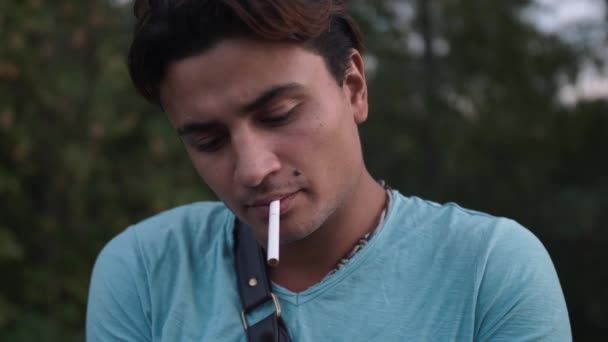 Um belo hispânico pega num cigarro e acende-o. Um tipo cansado fuma um cigarro de camisa azul. Homem tem ponto de beleza marca de nascença bem sobre o lábio
 - Filmagem, Vídeo