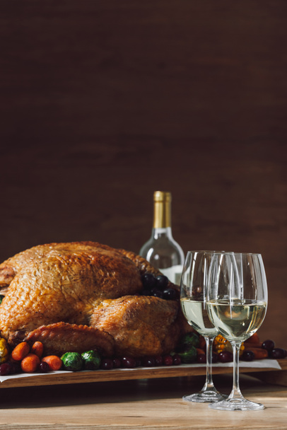 close up view of traditional roasted turkey, vegetables and glasses of wine for thanksgiving dinner on wooden tabletop - Photo, Image