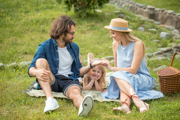 happy Family picnicking outdoors with their cute daughter, blue clothes, woman in hat - Photo, image