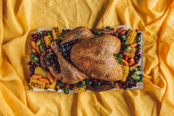 top view of roasted festive turkey and vegetables on tabletop with yellow tablecloth, thanksgiving holiday concept - Photo, Image