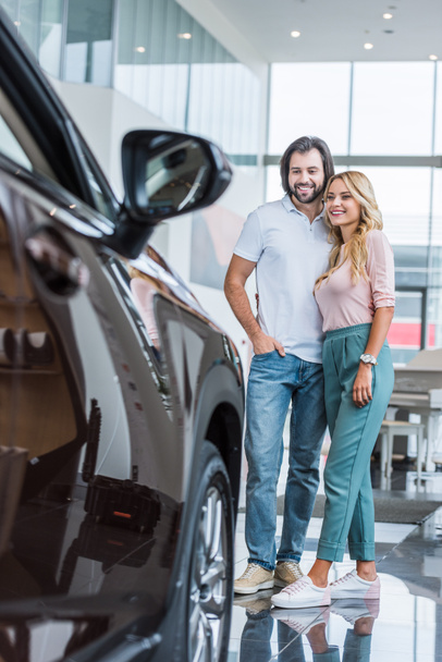 happy couple looking at new automobile at dealership salon - Photo, Image
