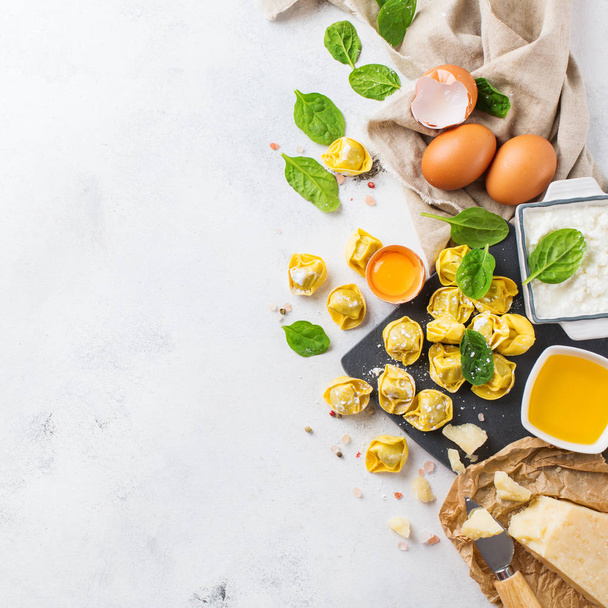 Assortment of italian food and ingredients, handmade tortellini with green spinach and ricotta cheese on a cutting board on a kitchen table. Top view flat lay copy space background - Photo, Image
