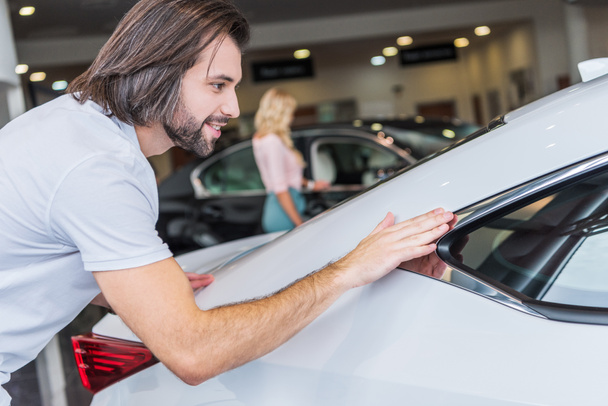 selective focus of man checking automobile with girlfriend on background at dealership salon - Foto, imagen
