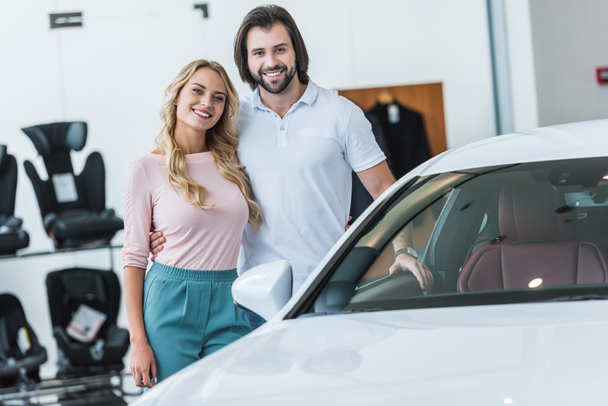 Porträt eines glücklichen Paares beim Umarmen am Neuwagen im Autohaus-Salon - Foto, Bild