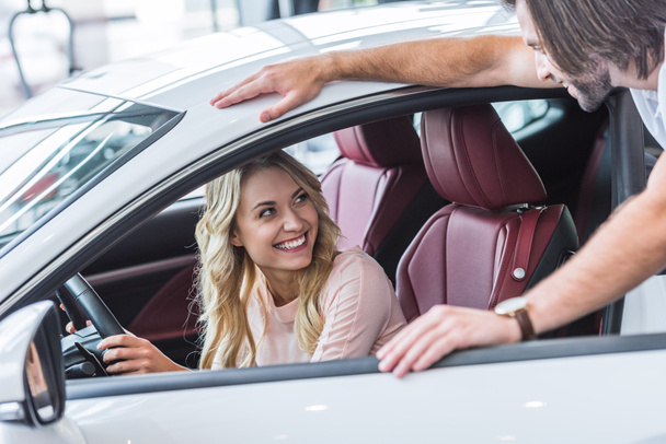 cheerful young couple with new car in auto salon - Photo, Image