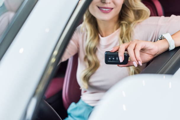 partial view of woman with car key in hand sitting in new car in dealership salon - 写真・画像