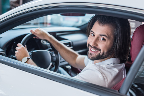 smiling bearded man sitting in new car for test drive in dealership salon - Photo, image
