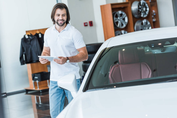 smiling man with digital tablet in hands at dealership salon - Foto, immagini