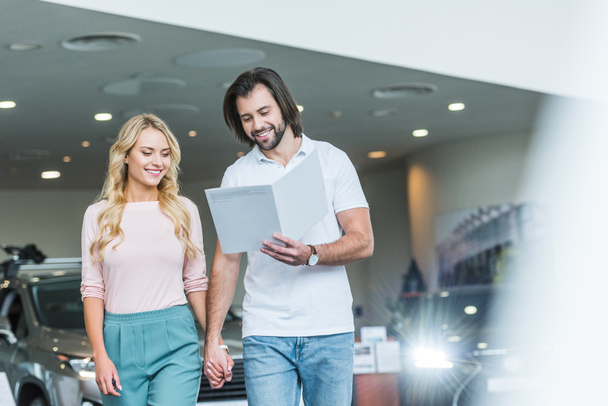 young couple with catalog buying car at dealership salon - Photo, Image