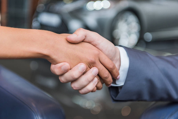 Schnappschuss von Autohaus-Verkäuferin und Kundin beim Händeschütteln im Autohaus - Foto, Bild