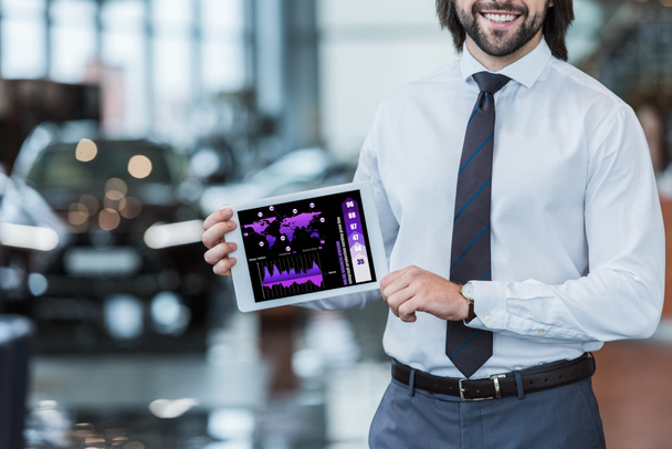 cropped shot of smiling dealership salon seller in formal wear showing tablet with graphic diagram in hands  - Photo, Image