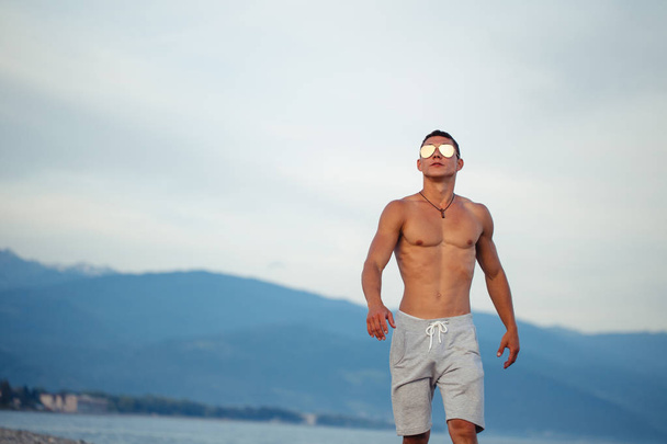 Masculine body man in sunglasses at beach with mountauns on background - Photo, image