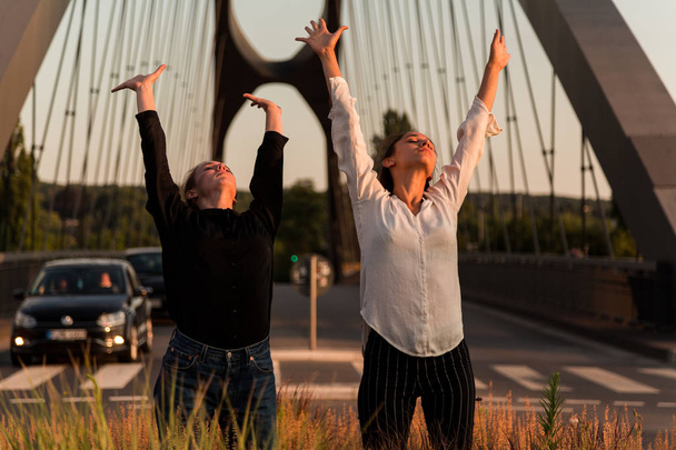 Predominan dos mujeres jóvenes bailando y posando en el camino de la ciudad con colores cálidos. Tres cuartos de longitud
.  - Foto, imagen